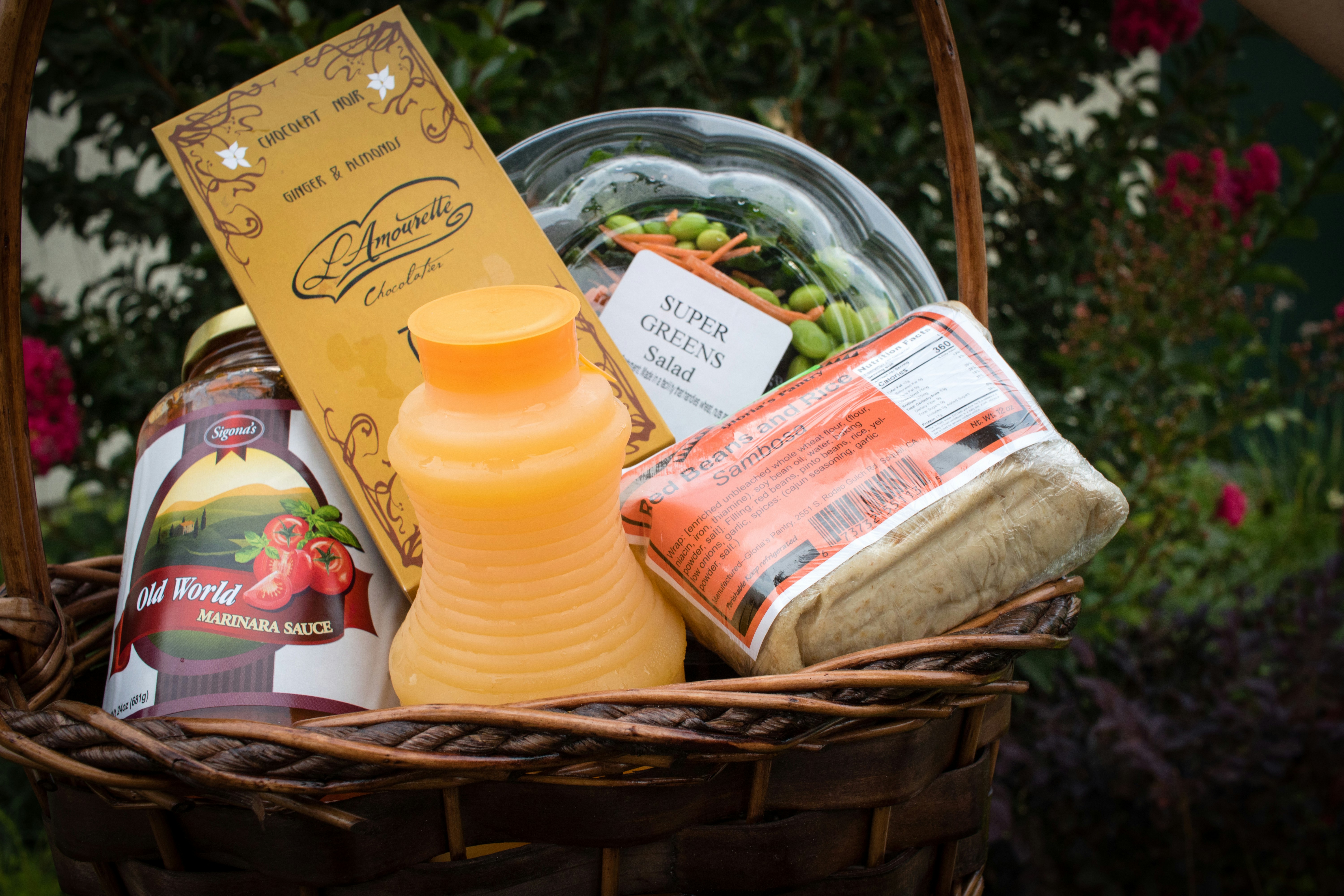 A custom gift basket packed with marinara, chocolate, juice, and fresh greens