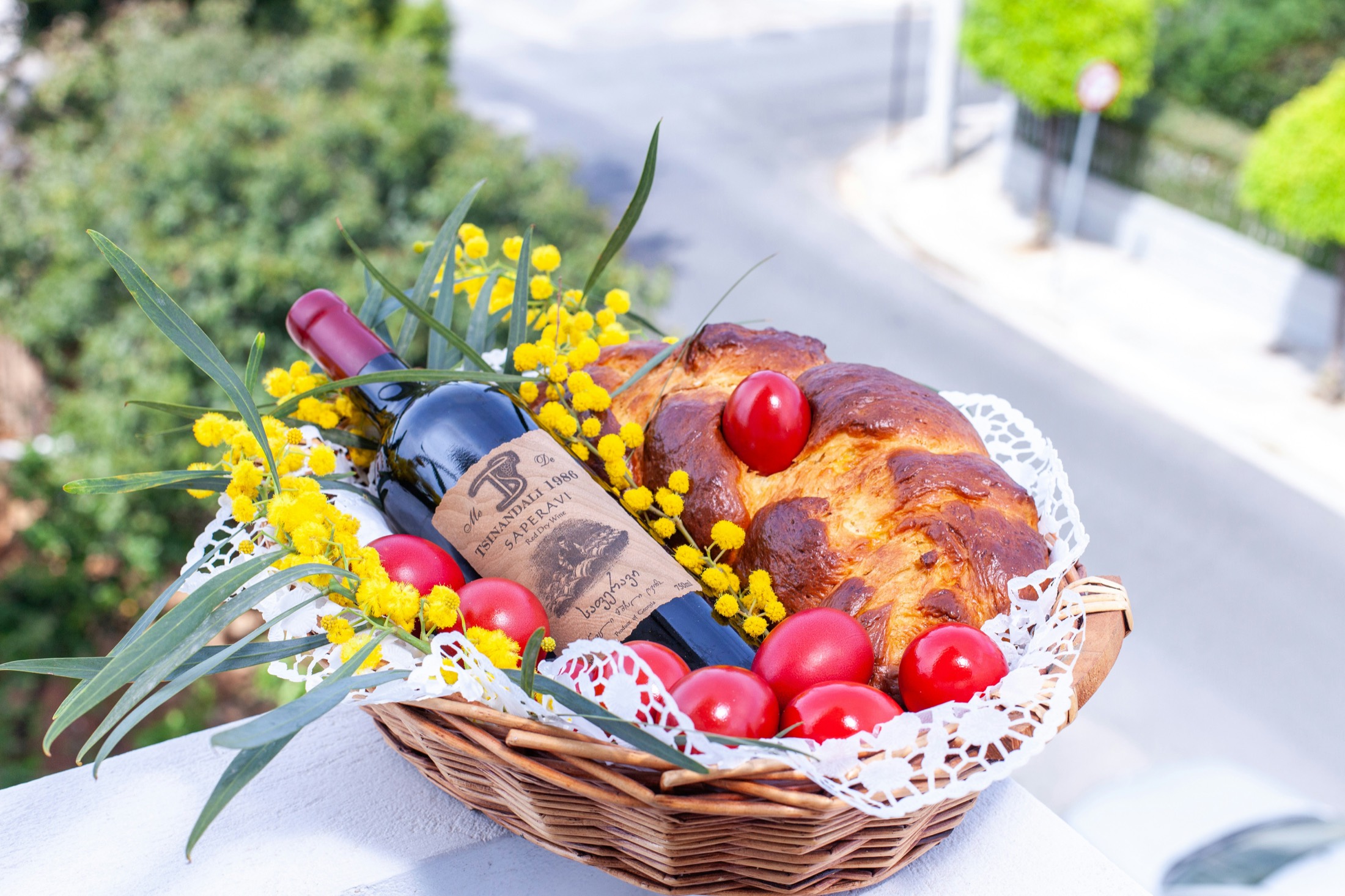 A gift basket of wine, fresh bread, and flowers arranged in a wicker basket