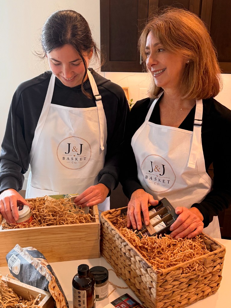 Joanne and Jennifer smiling while hand-packing gift baskets together.